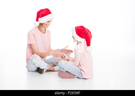 Happy mother and daughter wearing santa hats et jouant sur le plancher, isolé sur blanc Banque D'Images
