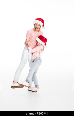 Smiling mother and daughter wearing santa hats et serrant sur noël, isolated on white Banque D'Images