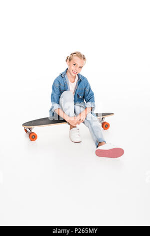 Petit enfant dans la grande chemise en jean assis sur un longboard, isolated on white Banque D'Images