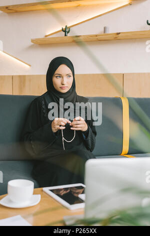 Une femme musulmane avec chapelet sitting on sofa in cafe Banque D'Images