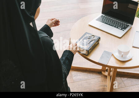 Femme musulmane moderne avec coran livre et les appareils numériques on table Banque D'Images