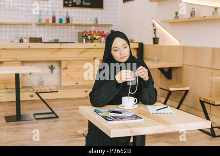 Une jeune femme musulmane avec chapelet assise seule dans cafe Banque D'Images