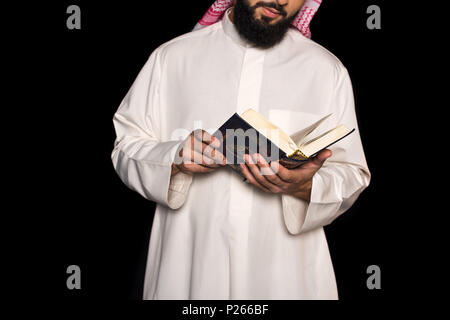 Cropped shot of Muslim man reading coran isolated on black Banque D'Images