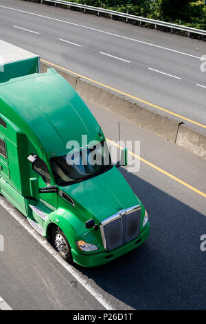 Gros camion vert American long haul semi truck avec semi-remorque tente de passer au large de la route tournant divisé avec des arbres sur l'arrière-plan pour la livraison de j Banque D'Images