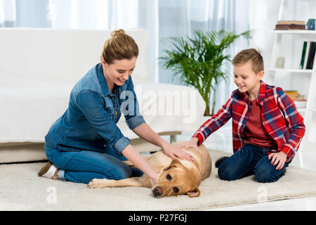 La mère et le fils de flatter leur chien alors qu'il a couché sur le plancher de salle de séjour Banque D'Images