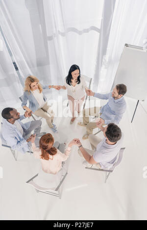 Vue supérieure de l'âge moyen des gens assis sur des chaises multiethnique et tenir la main à la thérapie de groupe Banque D'Images