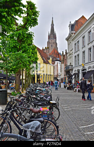 Les vélos sont laissés à côté d'une rue pavée typique avec theCatholic église Notre Dame dans le centre-ville distancem Bruges ou Brugge, Belgique Banque D'Images