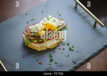 Délicieux sandwich aux œufs pochés, avocat et bacon sur un plateau d'ardoise (selective focus) Banque D'Images