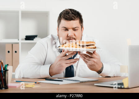 Homme d'embonpoint avec hamburger et frites in office Banque D'Images