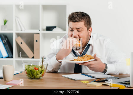 L'excès de businessman eating hamburger tandis qu'à la salade au Banque D'Images