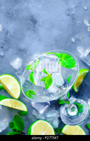 Verre à cocktail avec mojito cocktail Ingrédients, menthe, citron vert et des glaçons sur un fond de pierre. Rafraîchissement d'été mises à plat. La préparation de boissons concept Banque D'Images