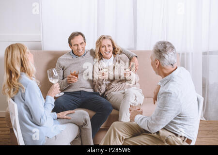 Amis avec verres en mains parlant, assis sur un canapé dans la salle à manger Banque D'Images