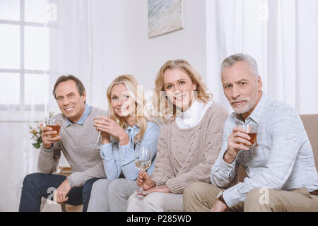 Happy friends avec des verres en mains assis sur un canapé et looking at camera Banque D'Images