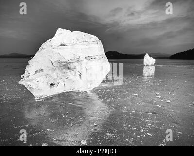 Des cubes de glace sur un terrain de réflexion sombre. Morceaux de glace haché rougeoyant et flocons de neige dans une forte contre-jour. La photographie en noir et blanc. Banque D'Images