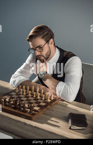 Jeune élégante businessman with hand on chin à la recherche au conseil d'échecs Banque D'Images