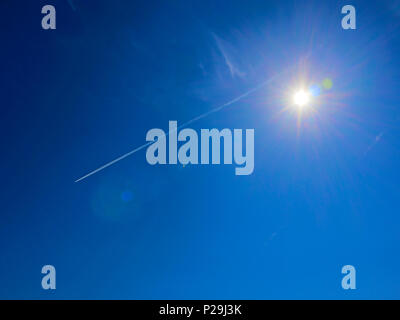 Grand soleil à l'aide de fusées éclairantes et auréole spectrale autour de contre ciel bleu avec des traces de jet blanc Banque D'Images