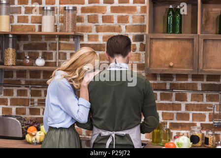 Vue arrière du femme serrant mari alors qu'il cuisine dans Cuisine Banque D'Images