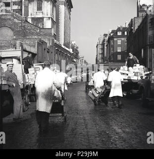 Années 1950, historique, du marché des porteurs dans une rue pavée déménagement en dehors de la caisses de poisson billingsgate market, Londres, Angleterre, Royaume-Uni. Banque D'Images