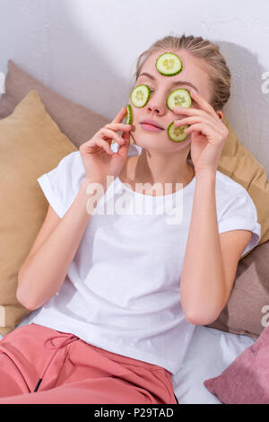 High angle view of young woman applying tranches de concombre sur le visage à la maison Banque D'Images