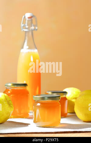 Gelée de coing faite maison et le jus dans une bouteille et en pots de verre avec coings sur une nappe de lin en plein soleil devant un fond orange et jaune Banque D'Images