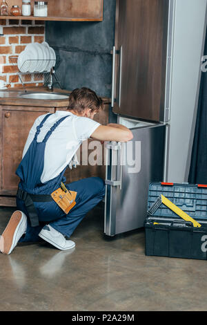 Vue arrière de fixation de protection workwear réparateur à réfrigérateur dans la cuisine Banque D'Images