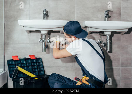 Vue arrière de jeune professionnel plombier lavabo fixation dans la salle de bains Banque D'Images