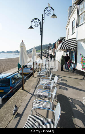 Front de plage à Lime Regis chaises en métal argent chaise lumières ombre oiseau pigeon sable bardeaux éclairage rue magasin de béton look élégant galets Banque D'Images