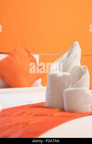 Origami serviette disposée sur un lit dans la chambre de couleur orange Banque D'Images