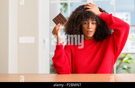 African American Woman eating chocolate bar à la maison a souligné avec la main sur la tête, choqué par la honte et la surprise face, en colère et frustrés. La peur et l'u Banque D'Images