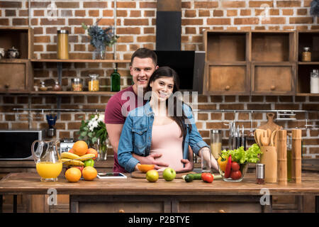 De belles jeunes femmes enceintes couple hugging and smiling at camera while cooking together Banque D'Images