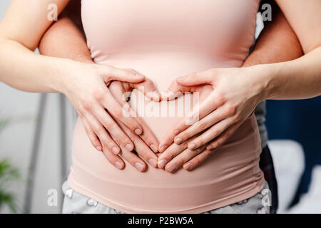 Cropped shot of young pregnant woman touching belly et main montrant le symbole de coeur Banque D'Images