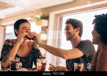 Femme de prendre une bouchée d'amis burger du restaurant. Groupe de jeunes ayant la nourriture dans un restaurant. Banque D'Images