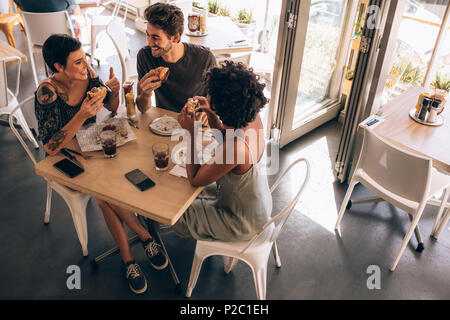 Portrait de trois jeunes amis avoir burger dans un restaurant. Petit groupe d'homme et de femmes assis autour de cafe table parler et manger. Banque D'Images