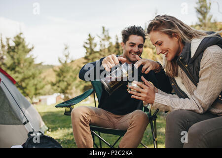 Belle jeune couple having coffee en camping dans la nature. Man pouring coffee in woman's cup. Banque D'Images