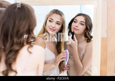 Belles jeunes femmes en pyjama appliquant le maquillage et à miroir à Banque D'Images