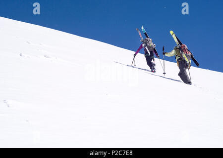 Une femelle et un mâle mountaineer transportant leurs skis de randonnée sur leurs sacs à dos et de la montée d'une pente de neige raide, sommet de Rocci Banque D'Images