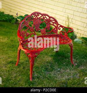 Fleuri rouge banc de jardin en fer forgé. Banque D'Images