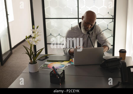 Senior graphic designer talking on mobile phone at desk Banque D'Images