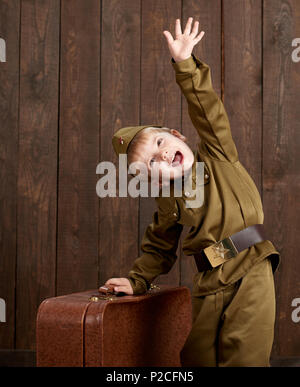 Les enfants garçon sont habillés en soldat en uniforme militaire rétro avec vieille valise, fond en bois foncé, style retro Banque D'Images