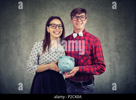 Cheerful l'homme et la femme à lunettes de la détention de monnaie banque et heureux avec budget commun smiling at camera. Banque D'Images