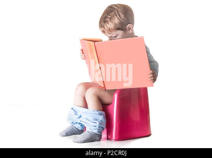 Tout-petit garçon assis sur le pot de chambre lecture livre d'histoires. Concept de formation de pot Banque D'Images