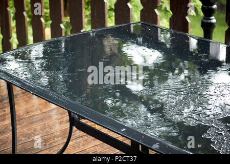La pluie rebondit sur un verre table de jardin au cours de l'été humide au Royaume-Uni Banque D'Images