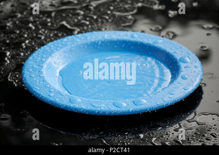 Plaque en plastique bleu noir assis sur table de jardin du remplissage avec de l'eau en raison de fortes pluies sur la journée d'été typique Banque D'Images