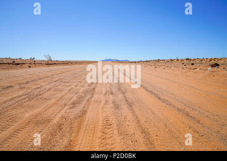 Les traces de pneus dans la poussière de la route de sable rouge s'étendant loin en avant à travers la Namibie paysage. Banque D'Images