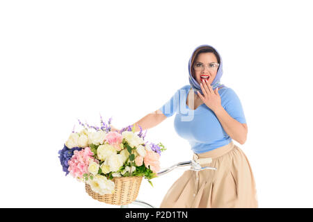 Surpris jeune femme assise sur le vélo avec panier de fleurs et smiling at camera isolated on white Banque D'Images