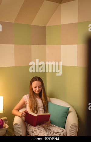 Girl reading book while sitting on chair Banque D'Images