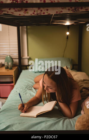 Girl lying on bed lors de l'écriture de journal dans la chambre Banque D'Images