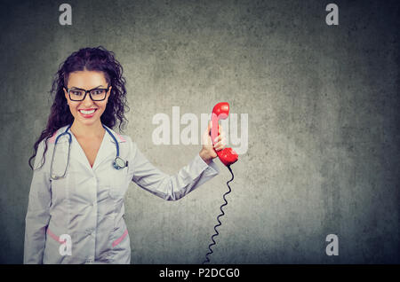 Pretty woman in white gown holding médical combiné rouge des lignes d'aide pour les personnes and smiling at camera Banque D'Images