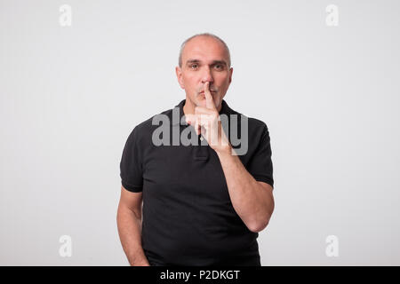 Beau vieil homme en t-shirt noir avec le doigt sur ses lèvres. Banque D'Images