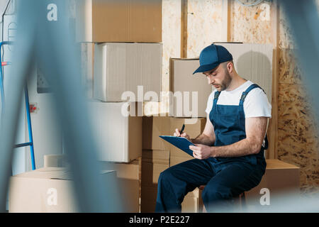 Delivery man filling Déclaration de la cargaison en position assise par des boîtes Banque D'Images